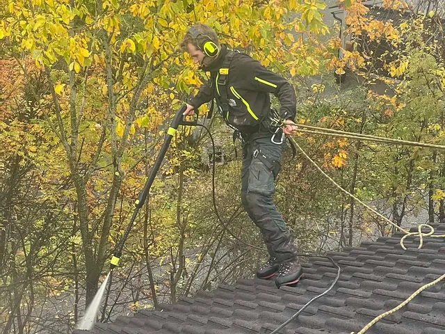 Arbeider med hørselsvern står sikret på tak og høytrykkspyler takstein i høstfarger.