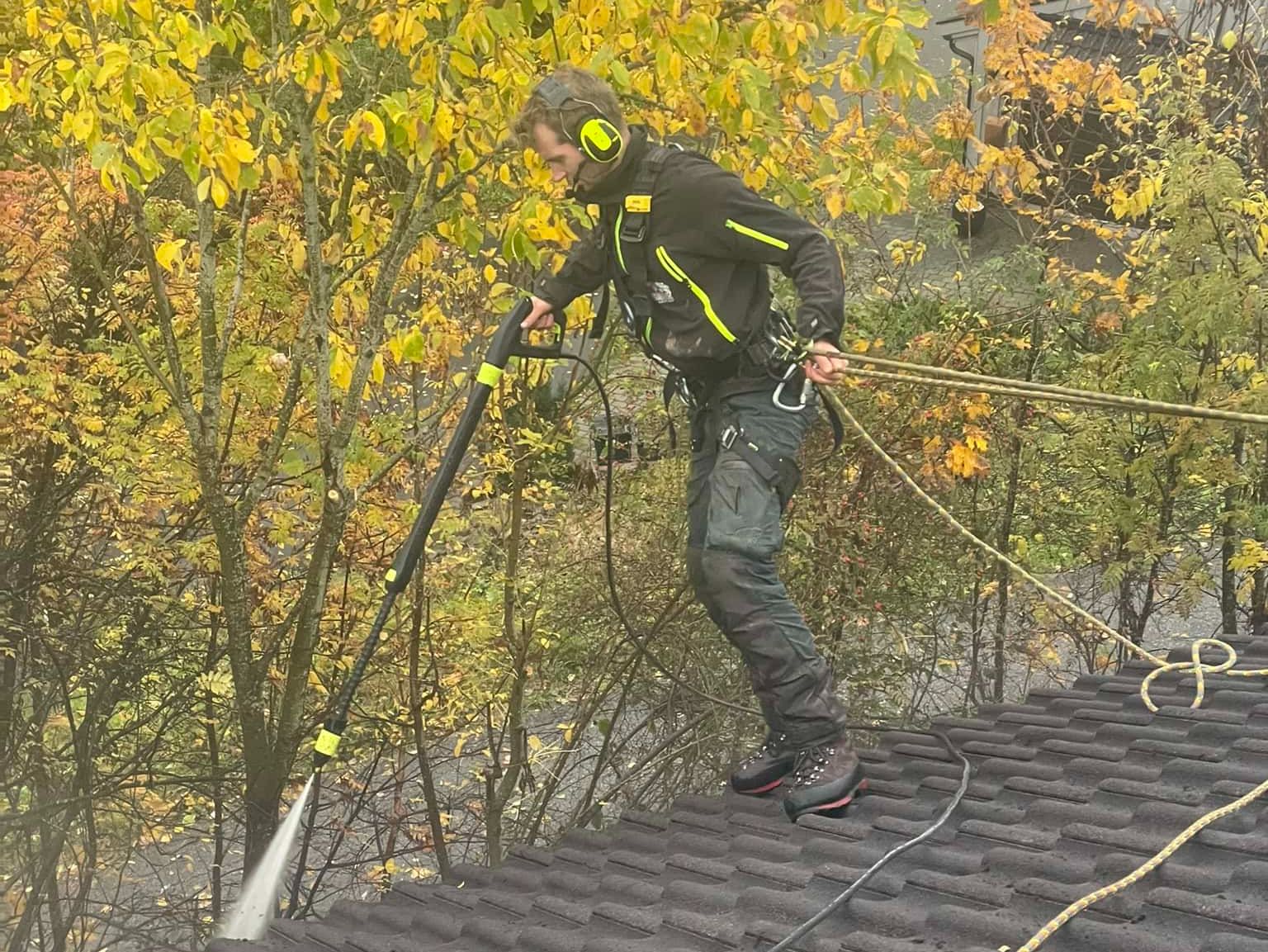 Arbeider med hørselsvern står sikret på tak og høytrykkspyler takstein i høstfarger.