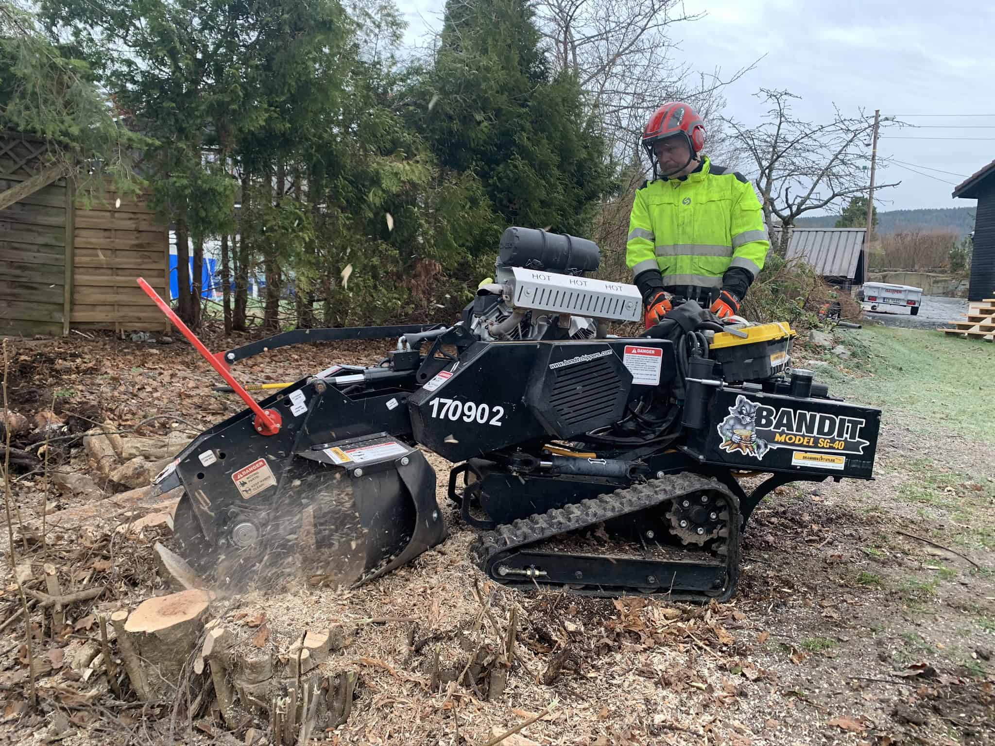 Arbeider bruker stubbe­freser for å fjerne en trestubbe i hage nær skog.